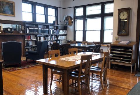 Image of the Guinn Room at Thorntown Public Library. There are two tables with multiple seating arrangements and a wall of genealogy reference information.