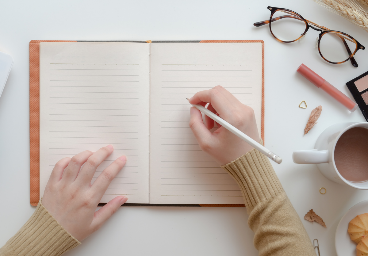 Image of an open notebook with hands preparing to write. Top view